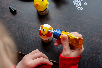 Image showing A girl decorates an egg for easter and glues funny eyes to it