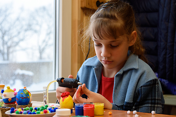 Image showing A girl glues a decorative element to crafts with a glue gun