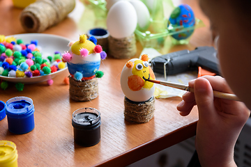 Image showing A girl draws a funny funny face on an Easter egg