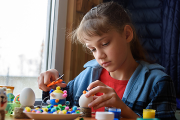 Image showing A girl sitting at a table makes Easter toys from chicken eggs