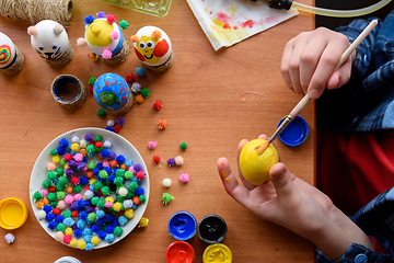 Image showing Top view of the desk and the hands of a child who paints festive easter eggs with brushes