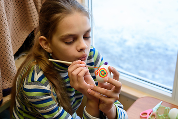 Image showing Girl paints Easter eggs while sitting at the table by the window