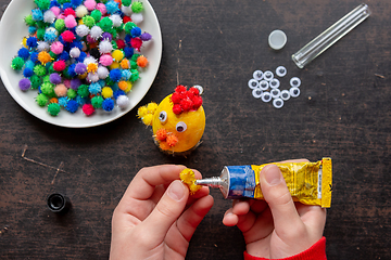 Image showing children\'s hands glue the wing to the chicken figure with glue from a tube