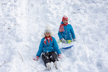 Image showing Two girls rolled down the hill and sitting in the snow joyfully look into the frame