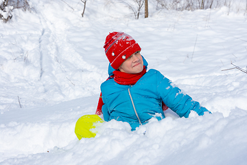 Image showing A girl sits in a snowdrift and looks funny at the top of the slide