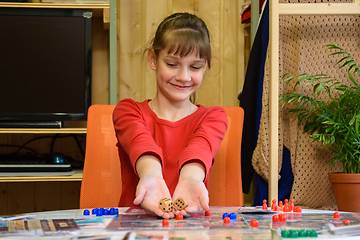 Image showing A girl throws large dice making another move while playing a board game at the table