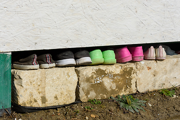 Image showing Under the house in the garden there is a row of various shoes