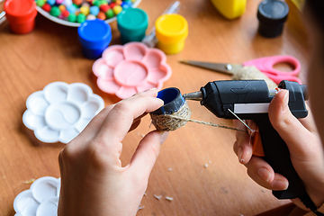 Image showing The girl\'s hands apply hot melt glue to the elements of the craft, gluing twine