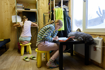 Image showing Two girls are doing homework at the computer table and the table on which the cat sleeps by the window in a small room of a country house