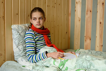 Image showing A sick girl sits in bed and looks tiredly out the window