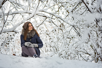 Image showing The girl sat down in a beautiful snowy forest and admires the beauty