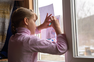 Image showing The girl copies the printed picture onto a blank sheet by attaching the picture to the window glass