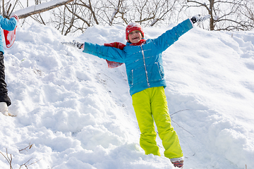 Image showing A happy girl stands on the slope of a slide in winter and throws her hands up rejoices at the first snow