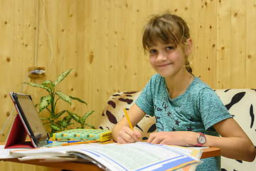 Image showing The girl learns her lessons at the table at home, was distracted and looked into the frame