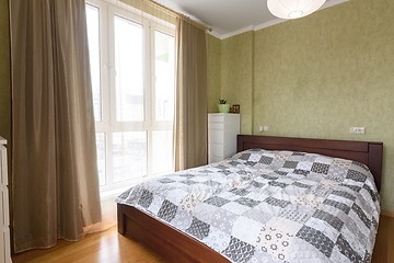 Image showing Bedroom interior with a large double bed and a large stained glass window with tulle and curtains