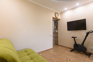 Image showing Fragment of the living room interior, in the foreground there is a sofa, on the back wall there is a TV and an exercise bike