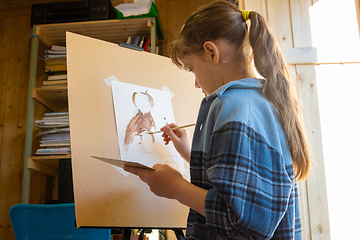 Image showing A ten-year-old girl draws with paints on an easel