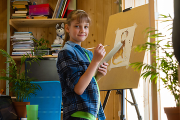 Image showing The girl was distracted from drawing on the easel and looked into the frame