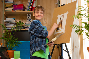 Image showing Happy girl at home draws on an easel and happily looked into the frame