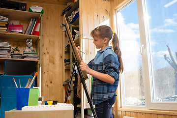 Image showing A ten-year-old girl draws on an easel by the wide window of the house