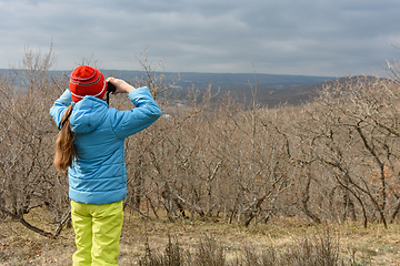 Image showing A girl in an autumn day looks through binoculars from the mountain, back view