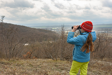 Image showing A girl examines a mountain landscape through binoculars, view from the back