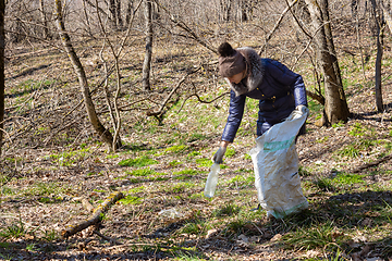 Image showing The girl collects garbage in the forest, took a plastic bottle and puts it in a bag