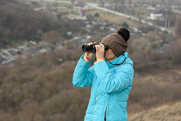 Image showing Girl looking through binoculars while standing on top of a mountain on a warm autumn day