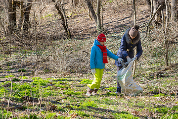 Image showing A girl and a woman collect garbage at the forest edge