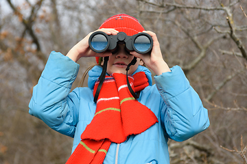 Image showing A girl looks through binoculars on a background of a winter forest, front view, close-up