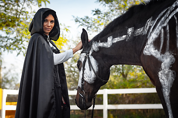 Image showing Portrait of a beautiful girl dressed in medieval style, a horse with a painted skeleton is standing next to