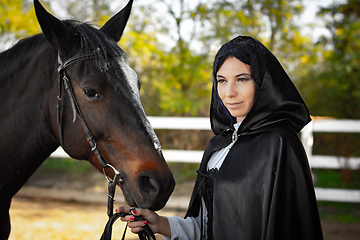 Image showing Portrait of a beautiful girl dressed in medieval style, the girl holds a horse by the bridle