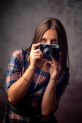 Image showing Girl photographer peeking out from behind the camera, half-length studio portrait on a gray background