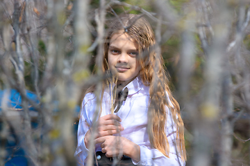 Image showing A girl stands with dried wildflowers, in the foreground blurred branches of bushes