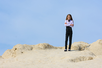 Image showing A girl in a white shirt with a bow tie stands on a mountain against the background of the sky