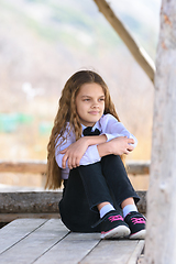 Image showing A girl sits on a wooden table and looks into the distance happily and dreamily