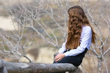 Image showing A girl sits on a wooden fence and looks away into the distance