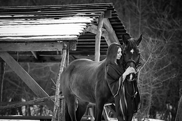 Image showing Beautiful girl hugs a horse near wooden buildings on a winter day, black and white photography