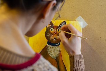 Image showing The artist paints a drawing of a cat on an easel with acrylic paints, a view from the artist\'s back