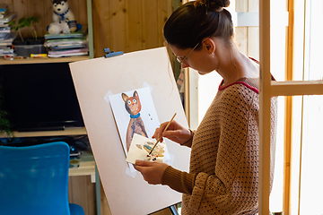 Image showing The artist mixes paints on a palette painting at home by the window