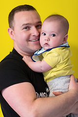 Image showing portrait of happy young father holding baby isolated on yellow