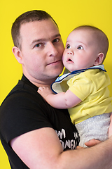 Image showing portrait of happy young father holding baby isolated on yellow