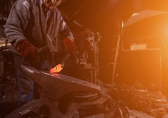 Image showing blacksmith manually forging the molten metal with sunlight throu