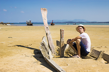 Image showing Young stranger sitting on the shattered boat and looking around