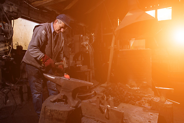 Image showing blacksmith manually forging the molten metal with sunlight throu