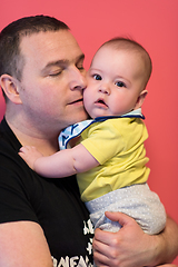 Image showing portrait of happy young father holding baby isolated on red