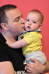 Image showing portrait of happy young father holding baby isolated on red