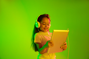 Image showing Portrait of little girl in headphones on green background in neon light