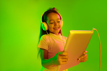 Image showing Portrait of little girl in headphones on green background in neon light