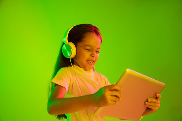 Image showing Portrait of little girl in headphones on green background in neon light